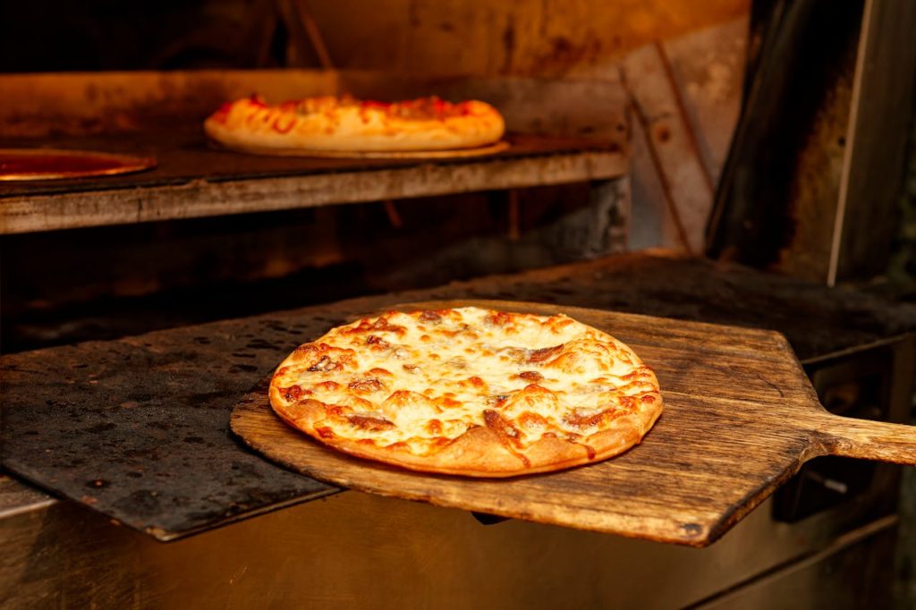 Pizza on a Wooden Pizza Peel near the Oven